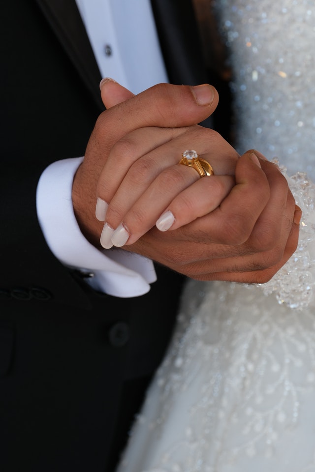 Bride and groom holding hands displaying diamond engagement ring with chunky gold band