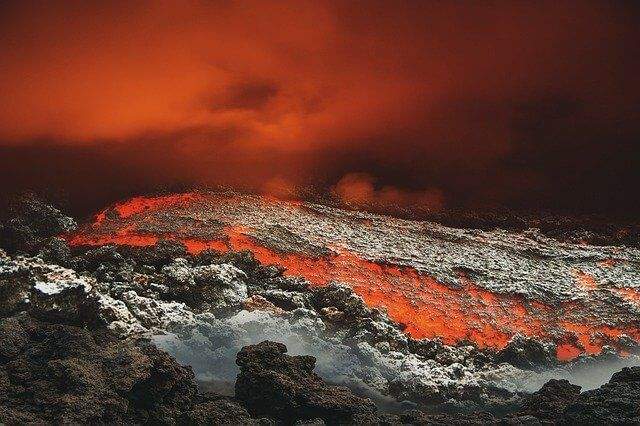 A dark cloudy red sky above lava and rocks.