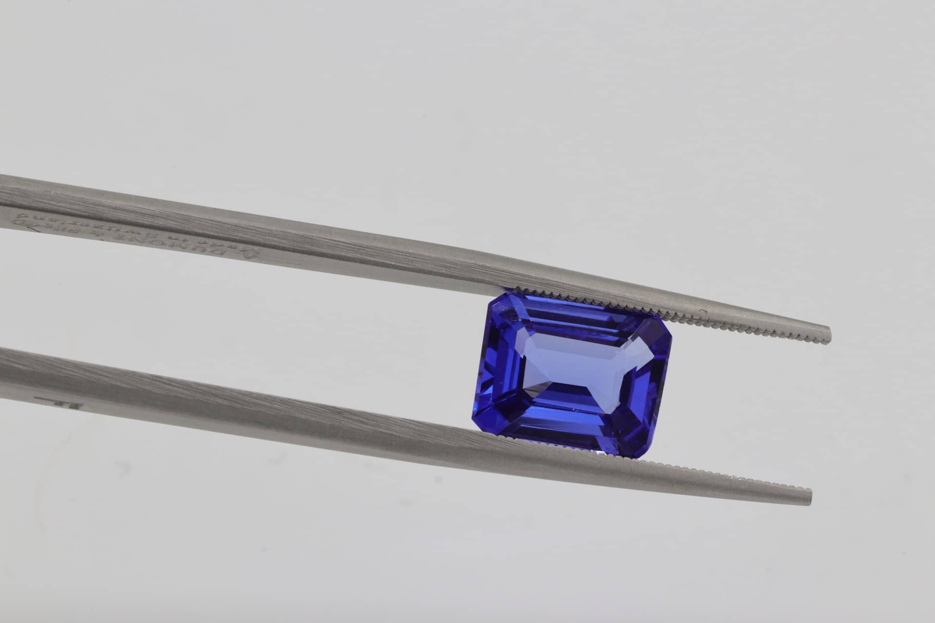 A pair of tweezers holding an emerald-cut blue sapphire